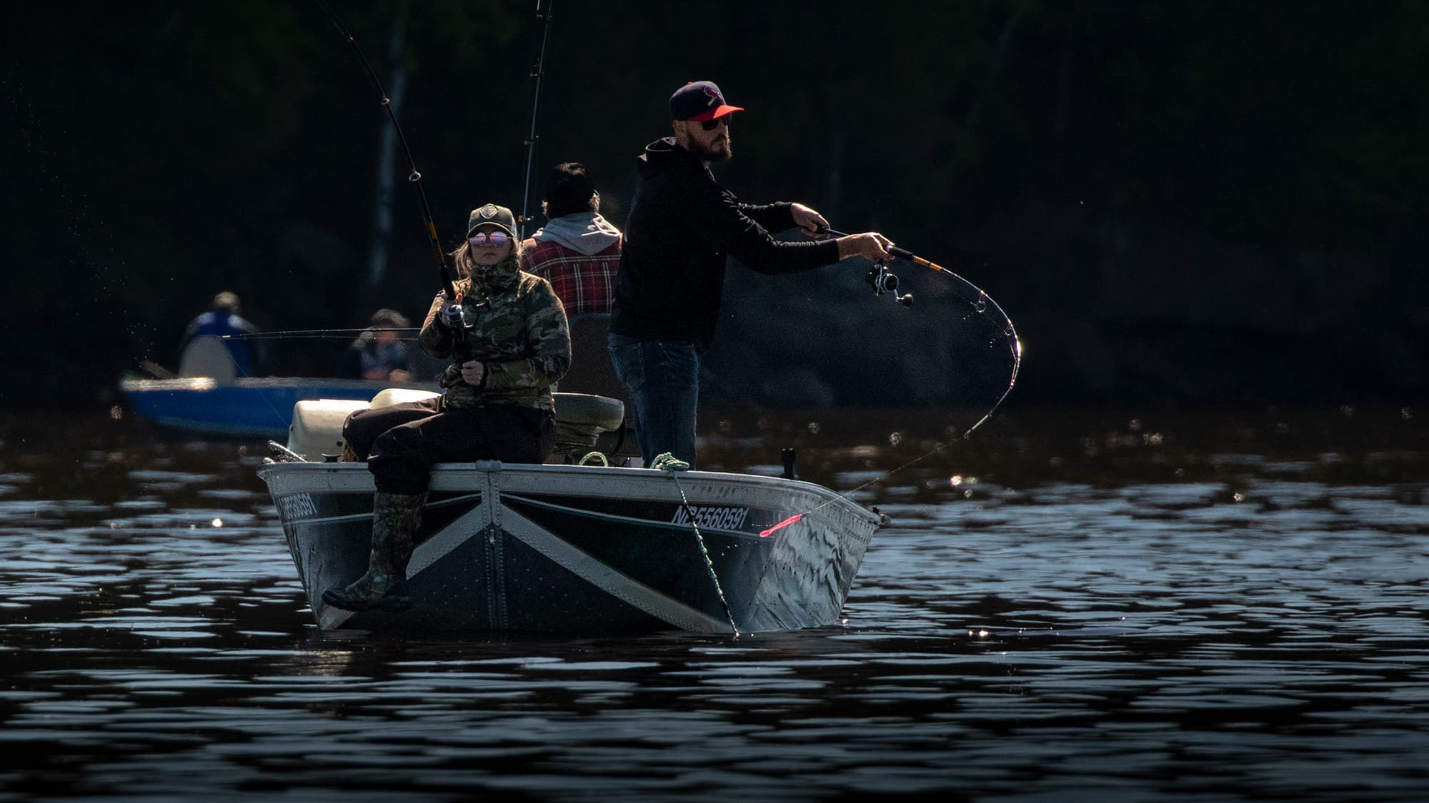 Three men on a boat, two of them are posing for a picture with a fish they caught while the third is taking a photo with his phone